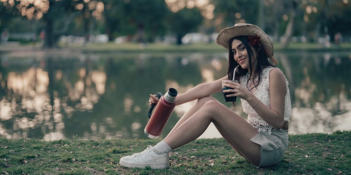 Young woman sitting by a lake drinking mate outdoors in Buenos Aires, Argentina.